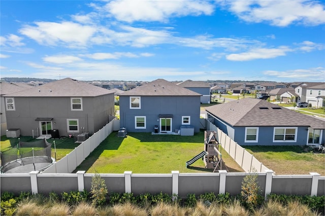 back of house with a fenced backyard, a yard, a residential view, central AC, and a playground
