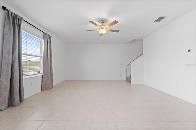 spare room featuring light tile patterned floors, ceiling fan, visible vents, and stairs