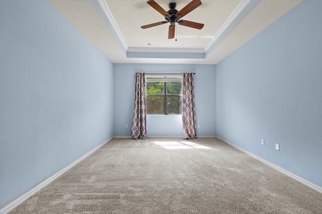carpeted empty room featuring ornamental molding, a raised ceiling, baseboards, and a ceiling fan