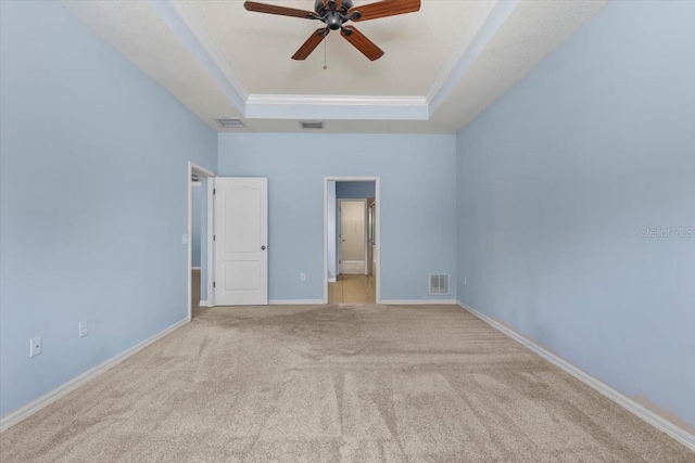unfurnished bedroom featuring a tray ceiling, carpet, visible vents, connected bathroom, and crown molding