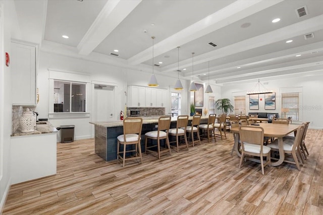interior space featuring light wood-style flooring, visible vents, stainless steel microwave, white cabinetry, and beamed ceiling