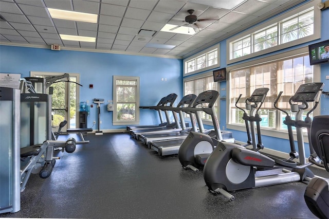 gym with a ceiling fan, a drop ceiling, and baseboards