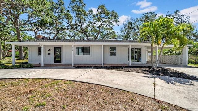 ranch-style house with board and batten siding, a porch, a chimney, concrete driveway, and a carport