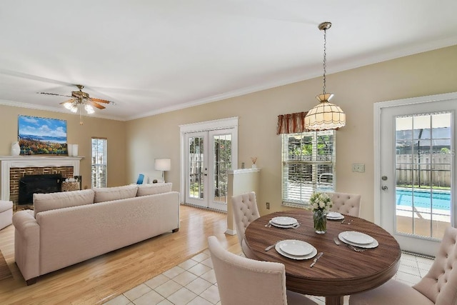 dining space with french doors, a fireplace, crown molding, ceiling fan, and light tile patterned floors