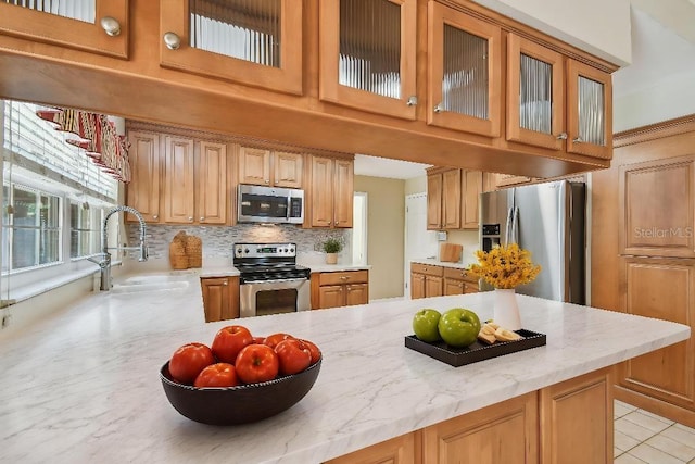 kitchen featuring glass insert cabinets, a sink, a towering ceiling, backsplash, and appliances with stainless steel finishes