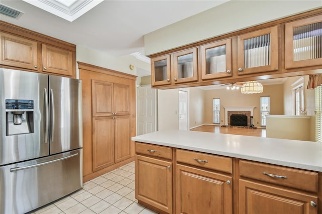 kitchen featuring brown cabinets, a fireplace, light countertops, light tile patterned floors, and stainless steel fridge with ice dispenser