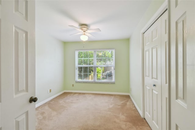 unfurnished bedroom with ceiling fan, light carpet, a closet, and baseboards