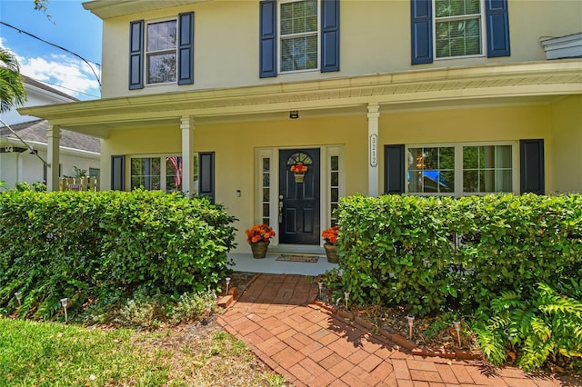 doorway to property featuring covered porch and stucco siding
