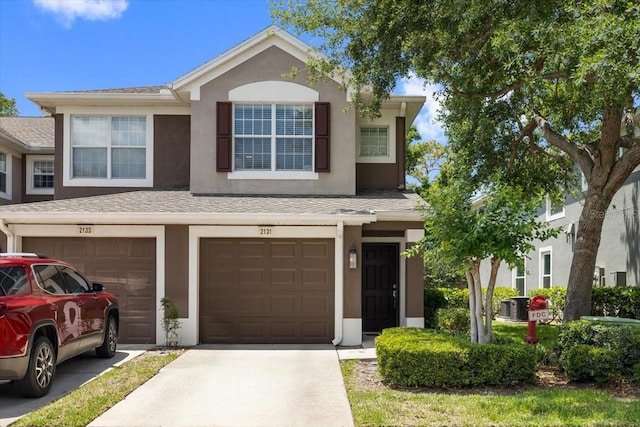 traditional home with a shingled roof, stucco siding, cooling unit, and driveway