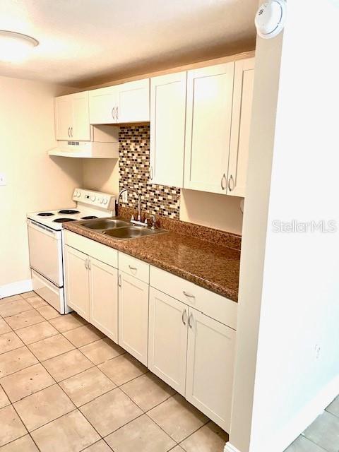 kitchen with light tile patterned floors, white electric range, under cabinet range hood, and a sink