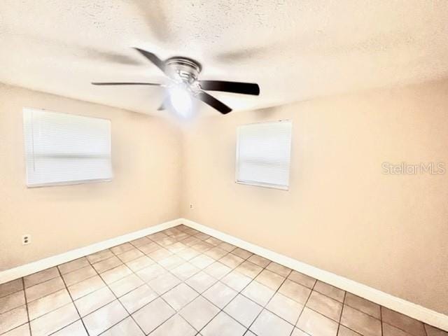 unfurnished room featuring a textured ceiling, ceiling fan, light tile patterned floors, and baseboards