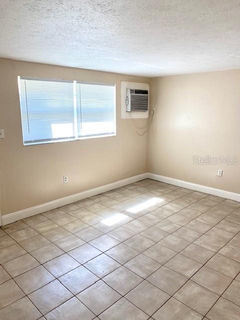 spare room with a textured ceiling, an AC wall unit, light tile patterned flooring, and baseboards