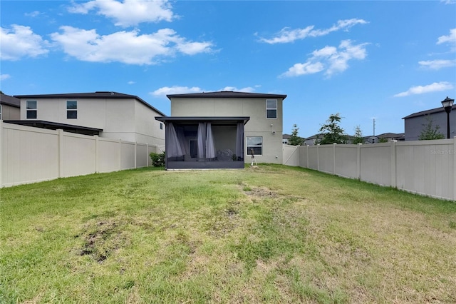 back of property with a lawn, a fenced backyard, a sunroom, and stucco siding