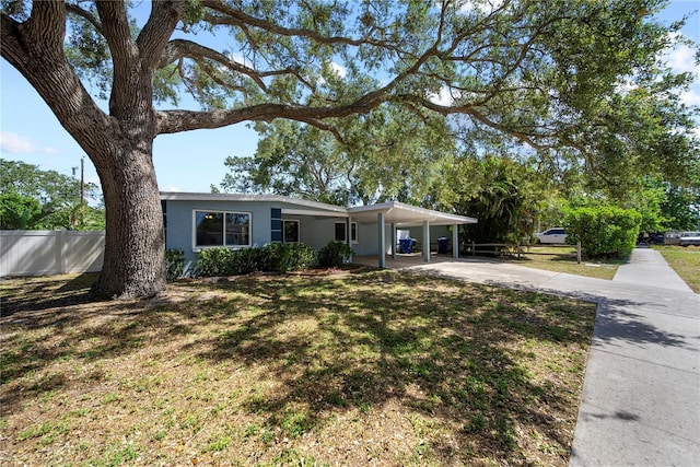 ranch-style house with a front lawn, fence, stucco siding, an attached carport, and concrete driveway