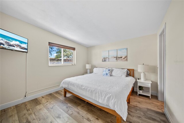bedroom featuring wood finished floors, baseboards, and lofted ceiling