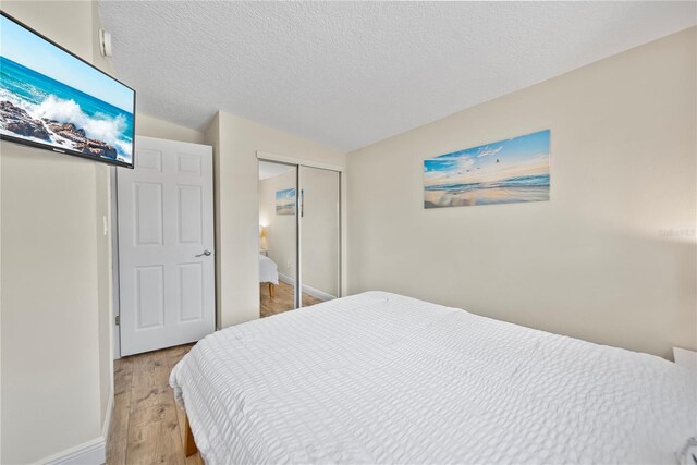 bedroom featuring baseboards, a textured ceiling, light wood-style flooring, and a closet