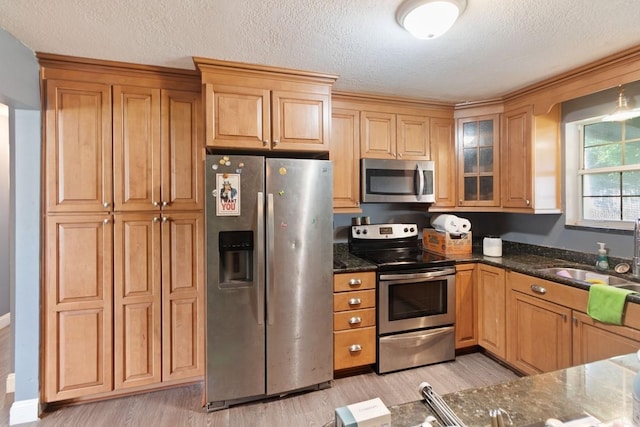 kitchen with dark stone countertops, stainless steel appliances, light wood-style flooring, and a sink