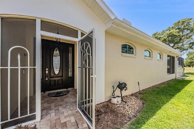 entrance to property featuring stucco siding and a lawn