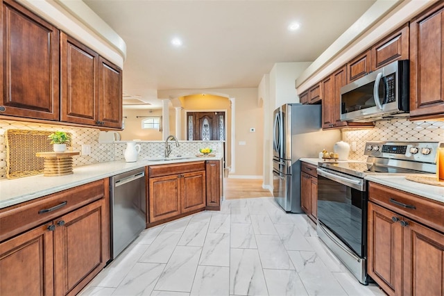 kitchen featuring a sink, stainless steel appliances, light countertops, ornate columns, and a peninsula