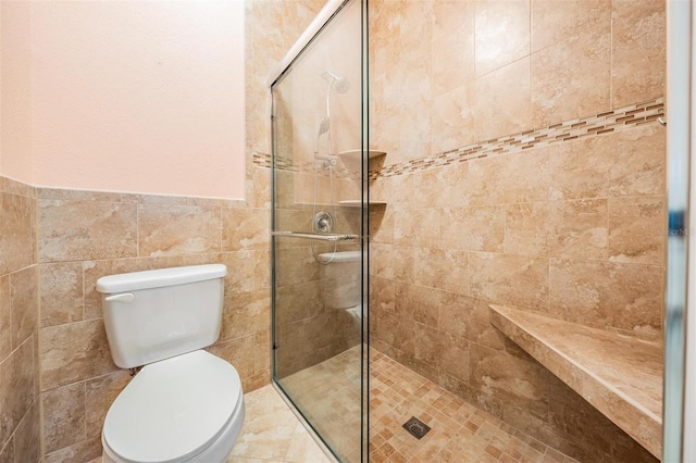 full bathroom featuring tile walls, wainscoting, tiled shower, and toilet