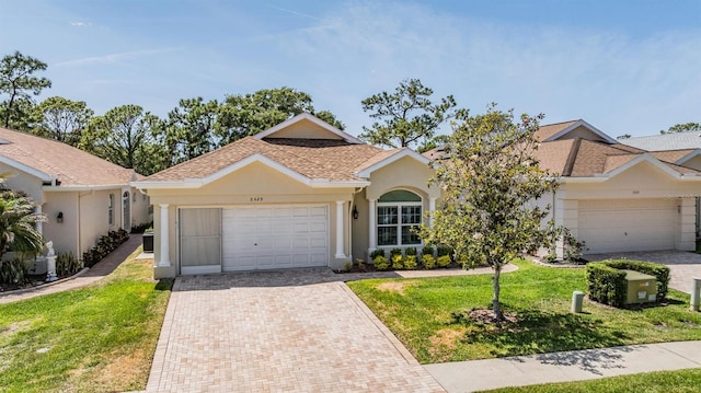 view of front of property featuring decorative driveway, roof with shingles, a front yard, stucco siding, and a garage