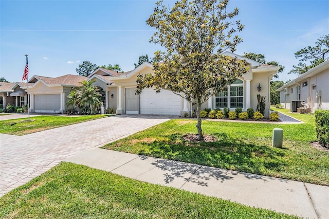 view of front of house with stucco siding, decorative driveway, central air condition unit, a garage, and a front yard