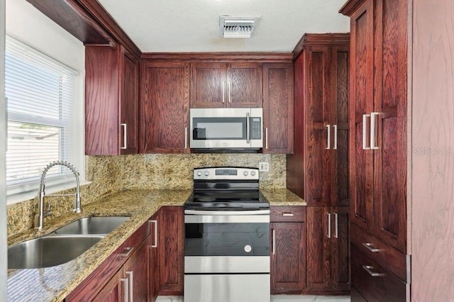 kitchen with light stone counters, reddish brown cabinets, a sink, and appliances with stainless steel finishes