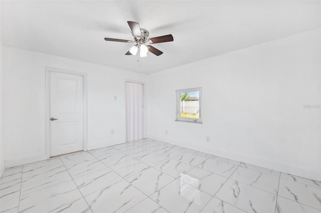 empty room with ceiling fan, marble finish floor, and baseboards