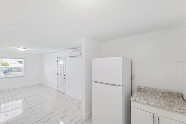 kitchen featuring baseboards, a wall unit AC, marble finish floor, and freestanding refrigerator