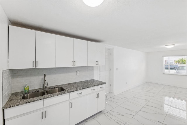 kitchen with dark stone counters, marble finish floor, a sink, and tasteful backsplash