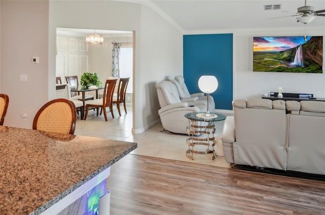living area featuring crown molding, ceiling fan with notable chandelier, baseboards, wood finished floors, and visible vents