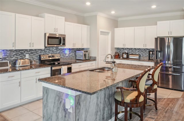 kitchen featuring a breakfast bar area, appliances with stainless steel finishes, a sink, white cabinets, and dark stone counters