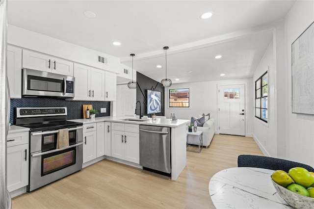 kitchen featuring a sink, appliances with stainless steel finishes, visible vents, light wood-type flooring, and a peninsula