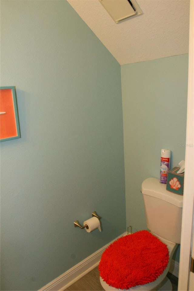 bathroom with baseboards, wood finished floors, vaulted ceiling, and toilet