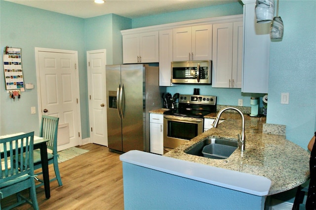 kitchen with a peninsula, light wood-type flooring, light stone counters, a sink, and stainless steel appliances