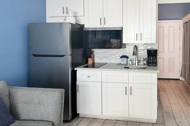 9980 Gulf Blvd Unit 603, Treasure Island, FL 33706 - kitchen with freestanding refrigerator, backsplash, black electric cooktop, light wood-style floors, and white cabinets