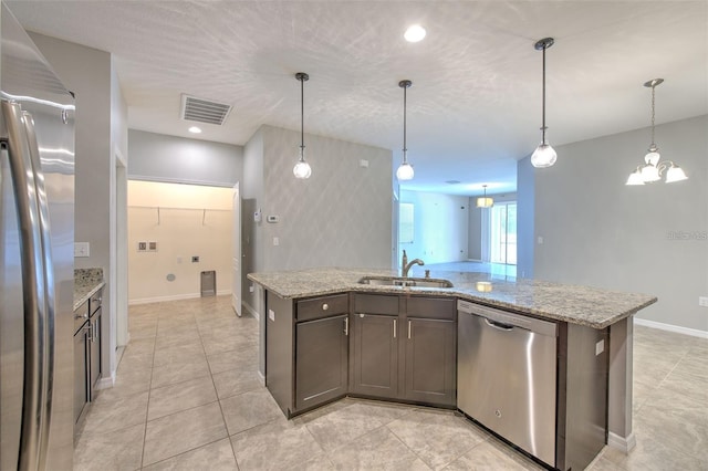 kitchen with visible vents, light stone countertops, a sink, decorative light fixtures, and stainless steel appliances