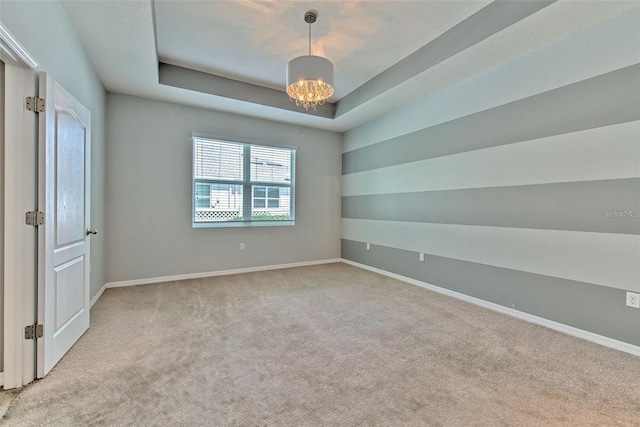 spare room with baseboards, carpet flooring, a tray ceiling, and an inviting chandelier
