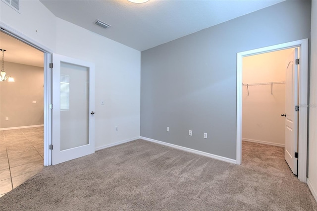 unfurnished bedroom with a walk in closet, baseboards, carpet floors, and visible vents
