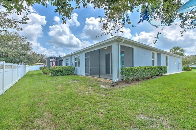 rear view of house with a lawn, fence, stucco siding, and a sunroom