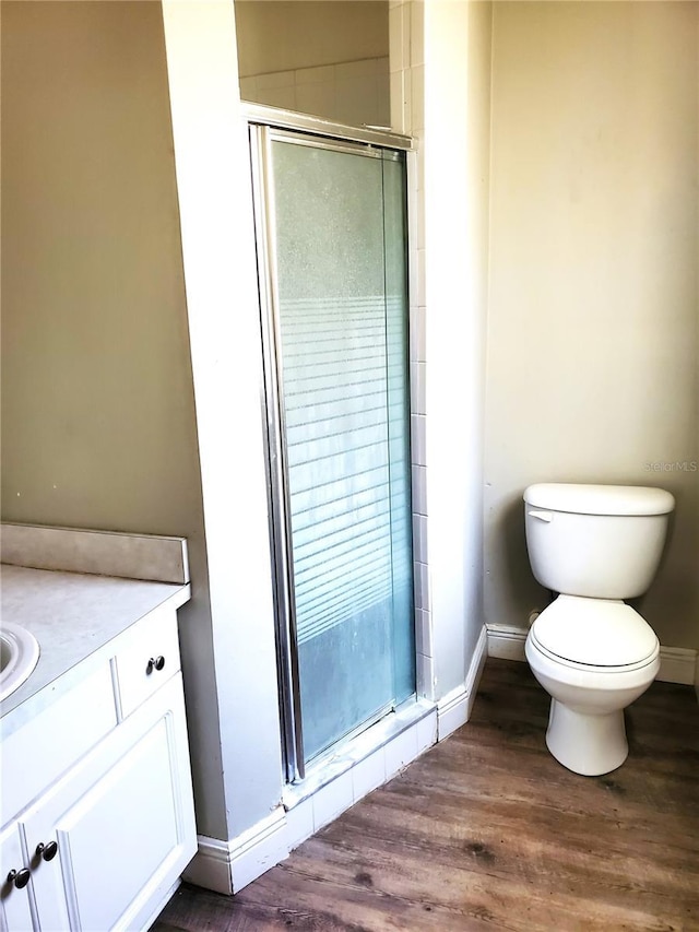 bathroom featuring wood finished floors, toilet, a stall shower, and baseboards