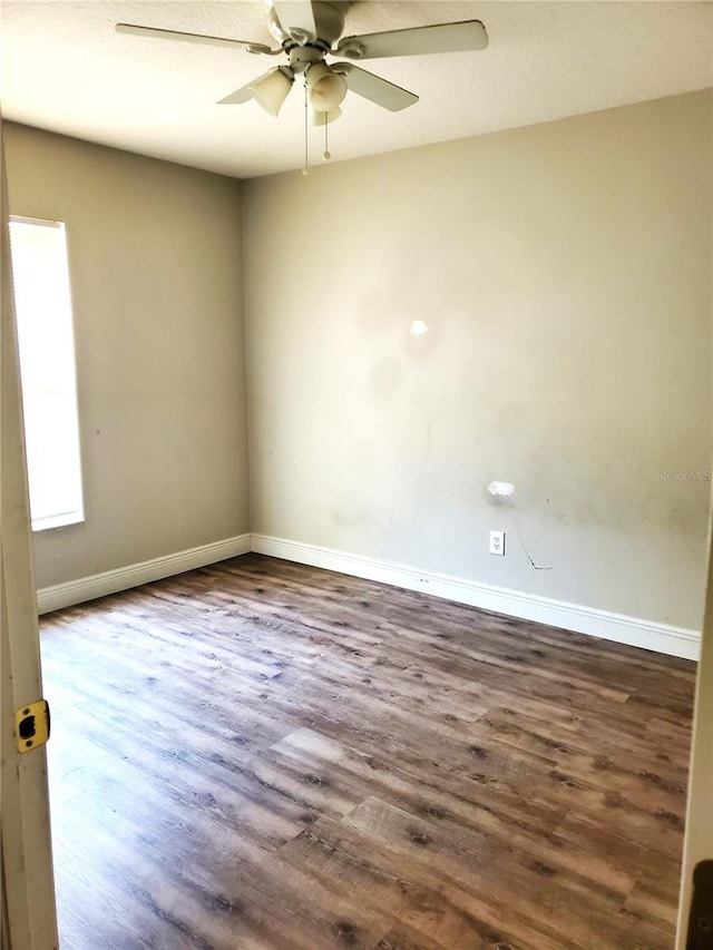 unfurnished room with ceiling fan, baseboards, and dark wood-type flooring