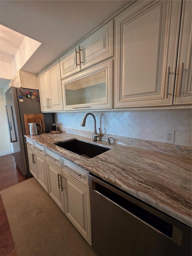 kitchen with backsplash, light stone countertops, a sink, stainless steel appliances, and dark wood-type flooring