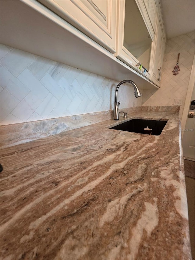 interior details featuring a sink, light stone counters, decorative backsplash, and cream cabinetry
