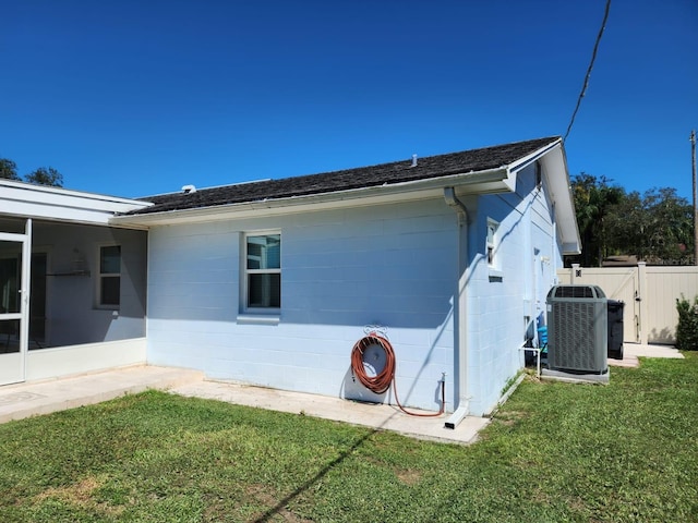 view of home's exterior featuring a lawn, central AC, fence, and concrete block siding