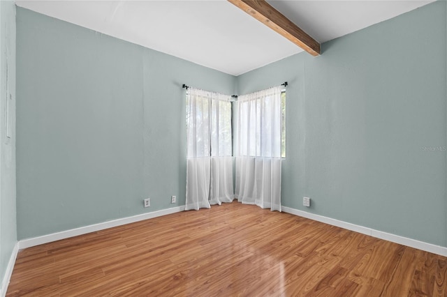 unfurnished room with baseboards, beam ceiling, and wood finished floors