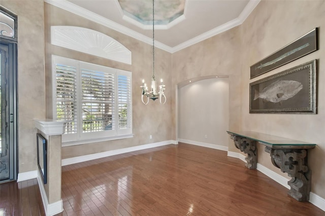 unfurnished dining area featuring a fireplace, baseboards, a chandelier, ornamental molding, and hardwood / wood-style floors
