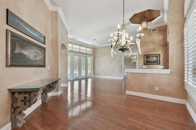 unfurnished dining area with visible vents, wood finished floors, baseboards, an inviting chandelier, and ornamental molding