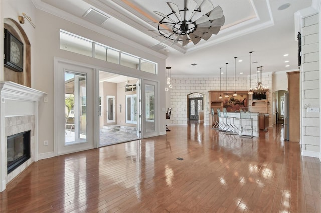 unfurnished living room with wood-type flooring, an inviting chandelier, a tiled fireplace, and visible vents
