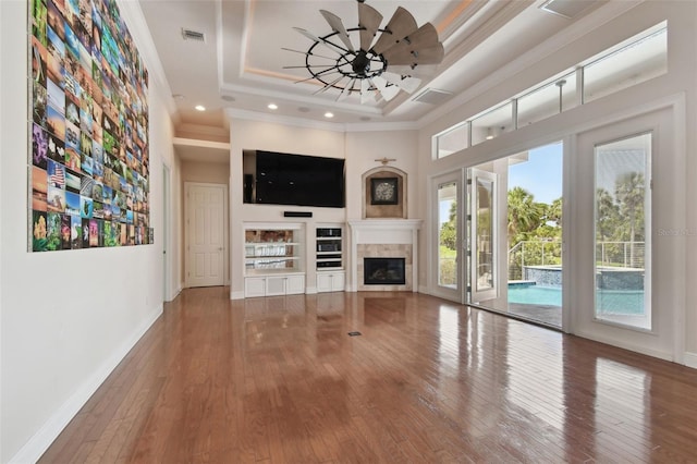 unfurnished living room with ceiling fan, baseboards, a tray ceiling, visible vents, and hardwood / wood-style flooring
